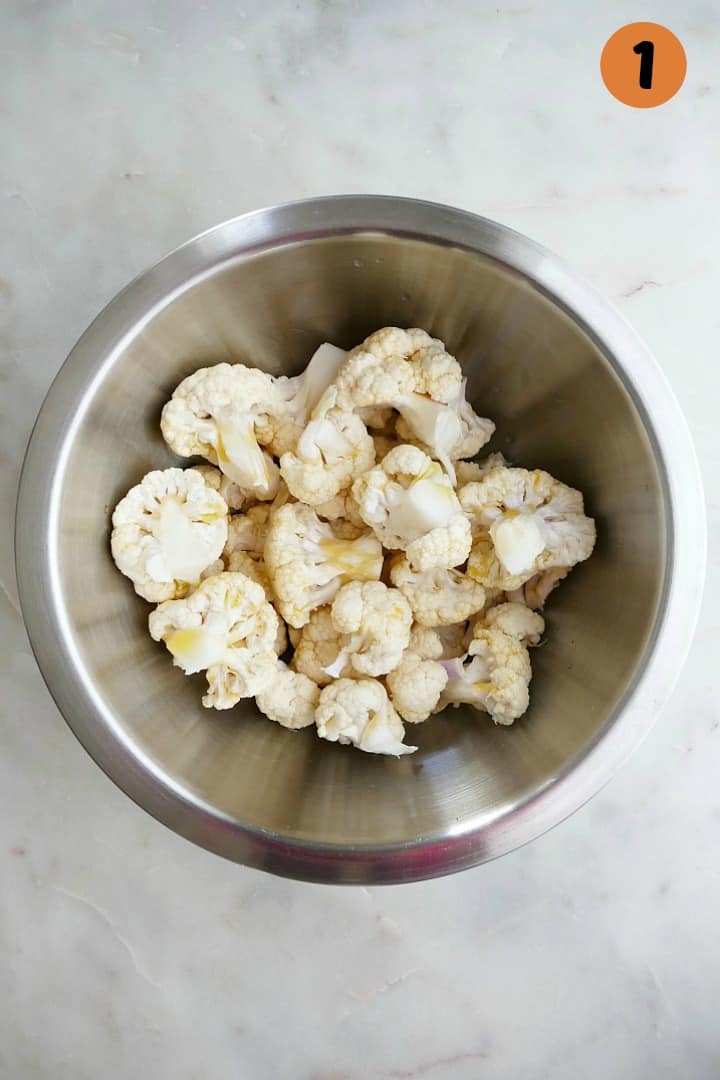 cauliflower florets in a silver mixing bowl tossed with olive oil