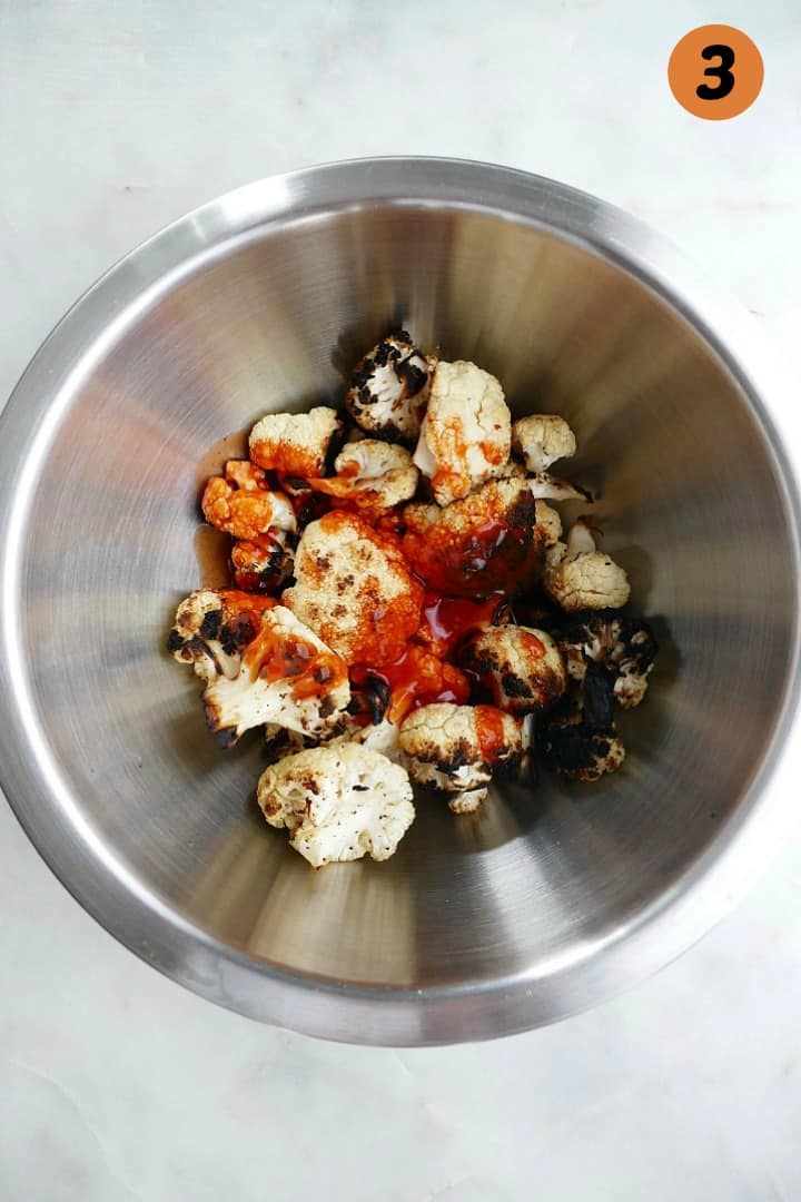 grilled cauliflower in a silver mixing bowl with buffalo sauce on top