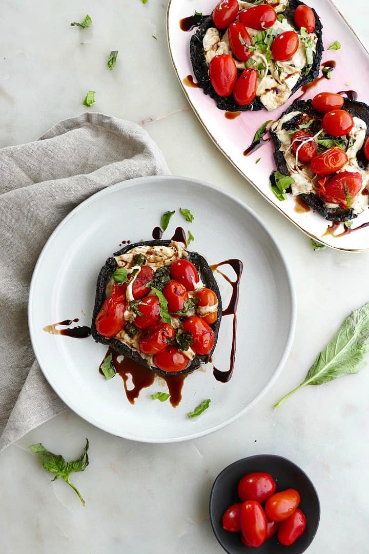 grilled stuffed mushrooms with caprese salad on a plate and tray on a white counter