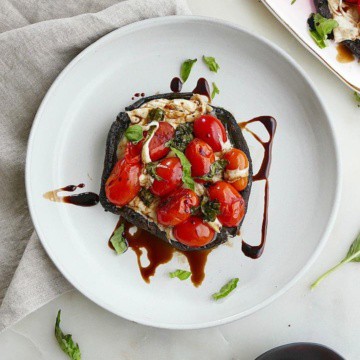 stuffed mushroom with caprese salad on a white plate on a counter