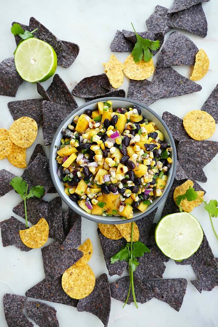 mango corn salsa in a gray bowl with blue and yellow chips surrounding it