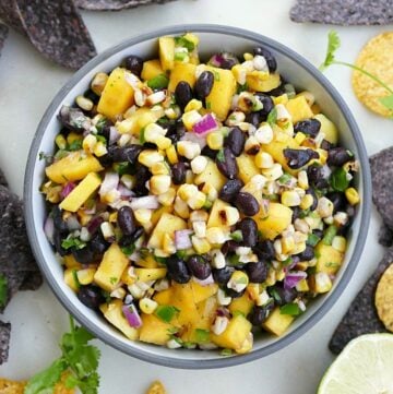 close-up of mango corn salsa in a gray bowl surrounded by chips and limes