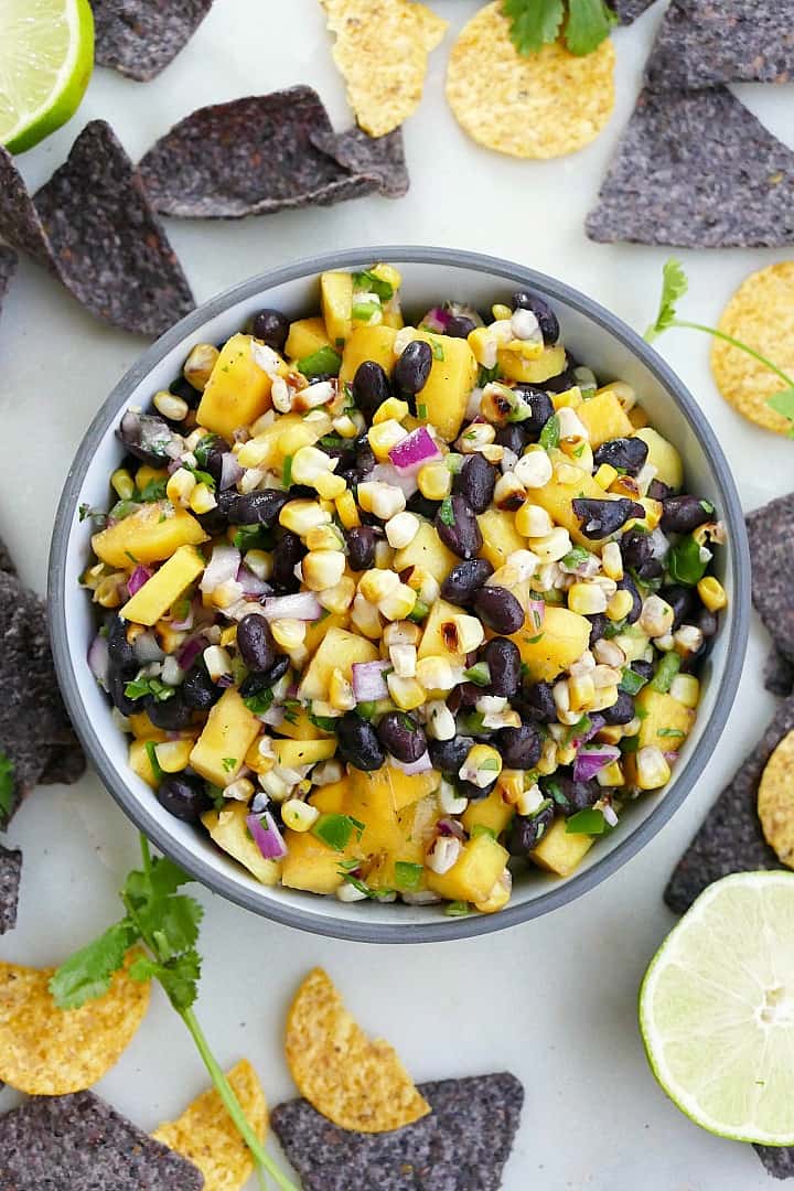 close-up of mango corn salsa in a gray bowl surrounded by chips and limes