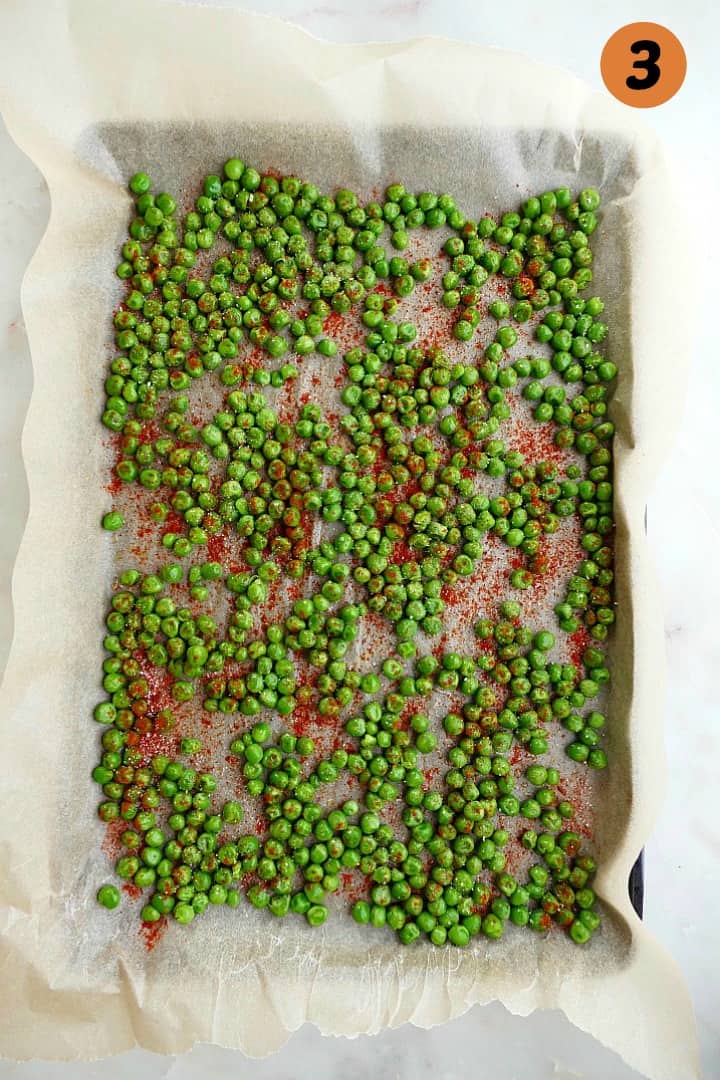 frozen peas tossed in spices spread out on a parchment lined baking sheet
