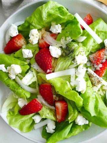 square image of strawberry goat cheese salad on a white plate on a counter