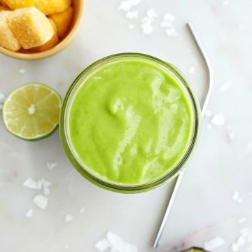 overhead shot of a creamy avocado green smoothie in between mango, lime, and avocado