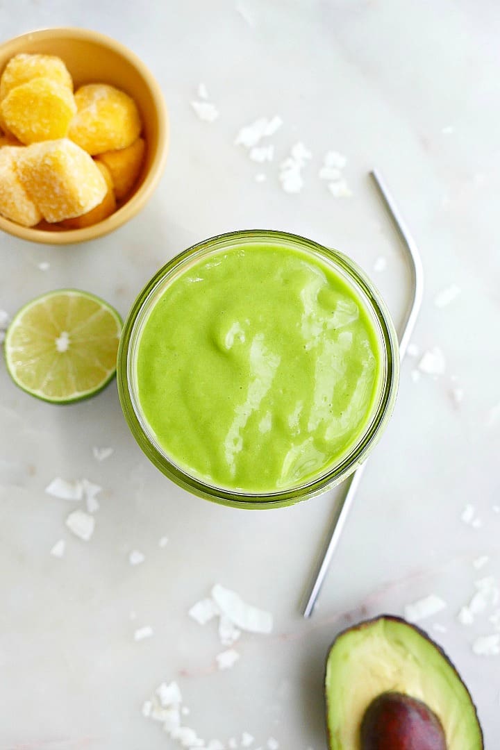 overhead shot of a creamy avocado green smoothie in between mango, lime, and avocado