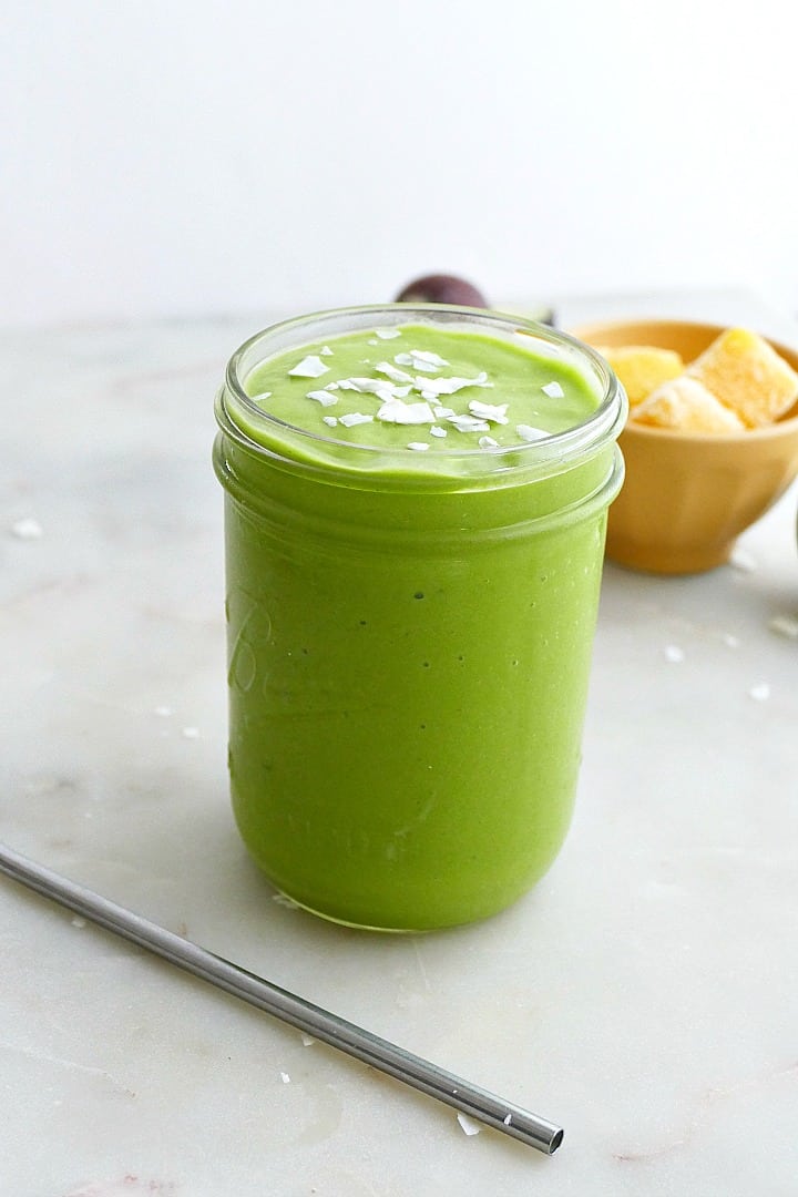 photograph of a green smoothie in a glass jar with mango in the background