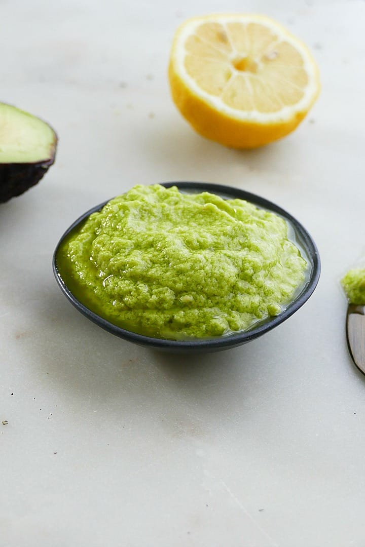 side view of garlic avocado spread in a black bowl with a lemon behind it