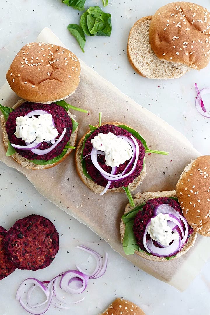 three beet black bean burgers on a piece of parchment paper with buns and toppings