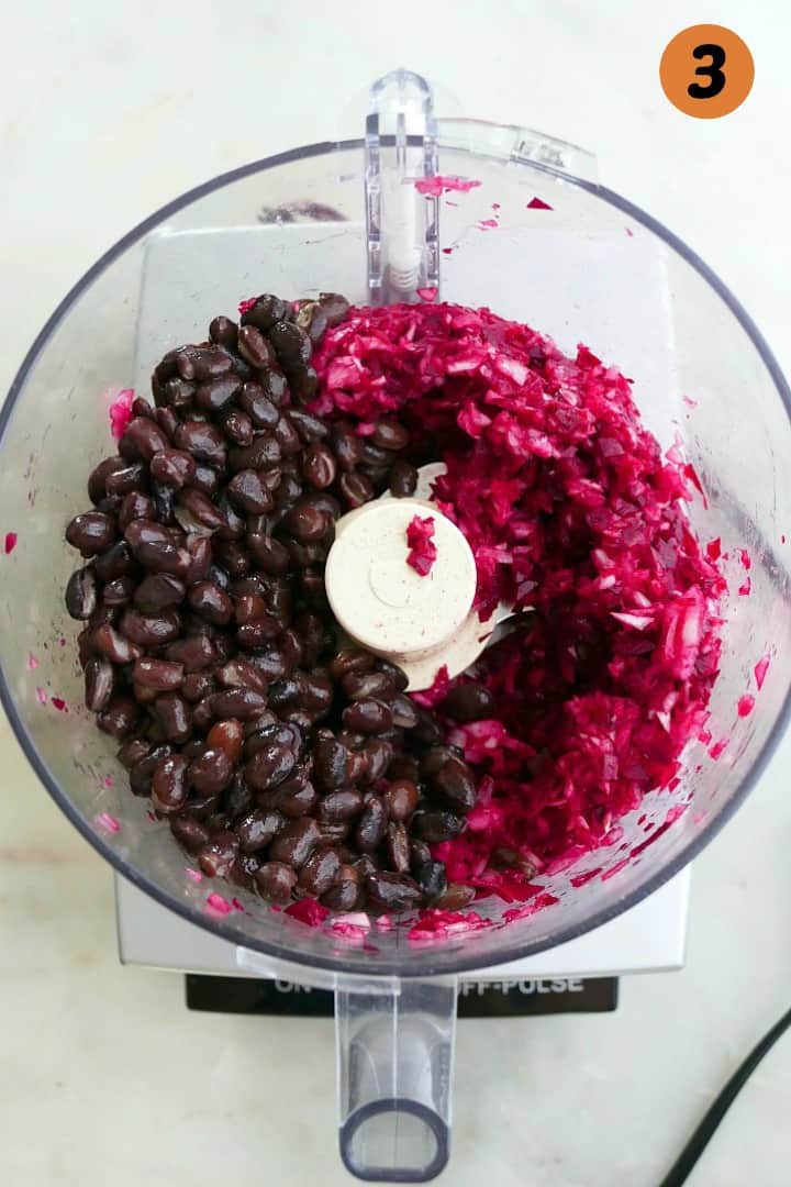 chopped onions and beets with whole black beans on top in a food processor