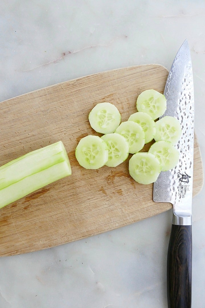 sliced cucumber on a cutting board with a chef's knife on a counter