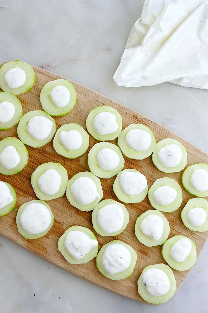 small cucumber canapes on a cutting board with whipped feta on top