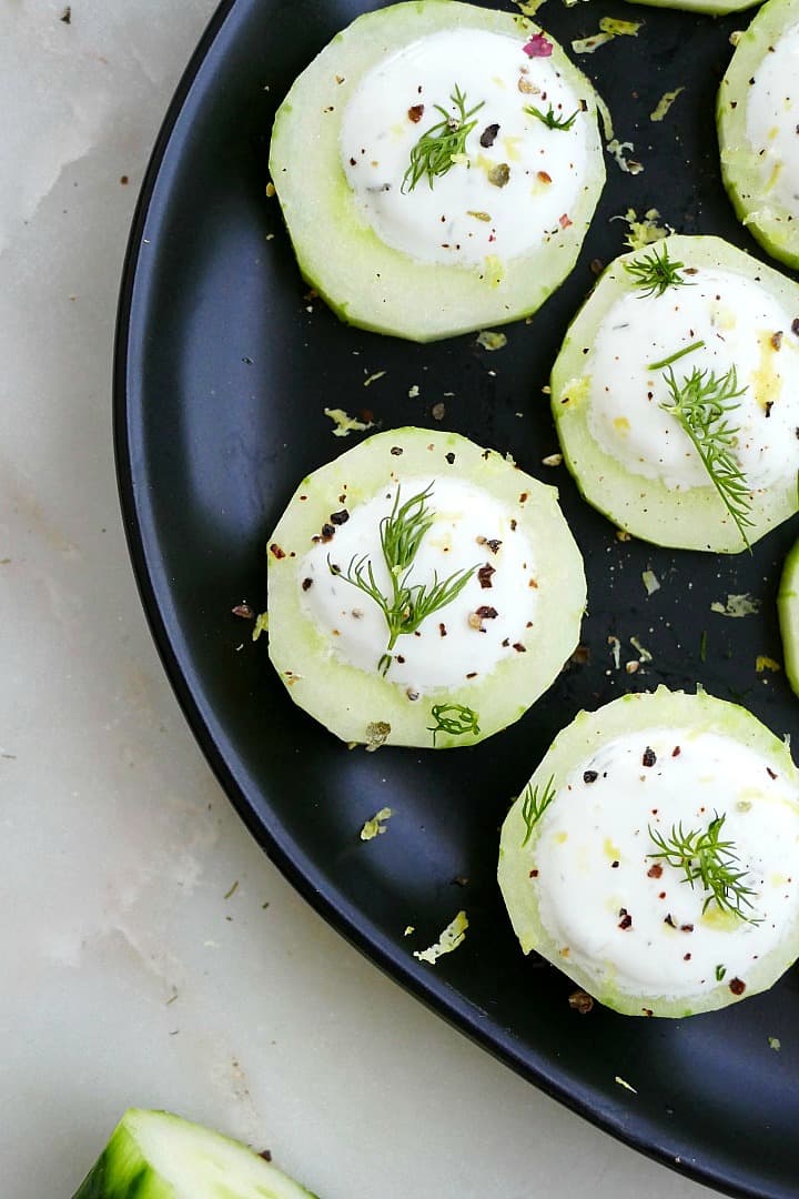 close up shot of 4 canapes on a black plate topped with dill and pepper