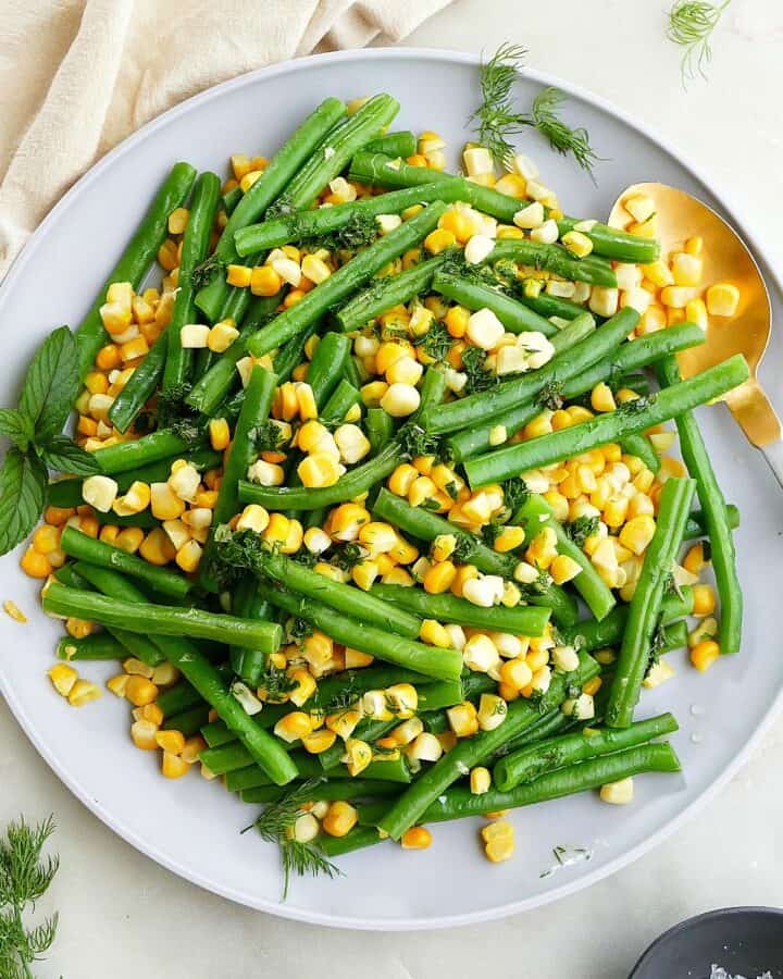 square image of green beans and corn on a gray plate with gold spoon