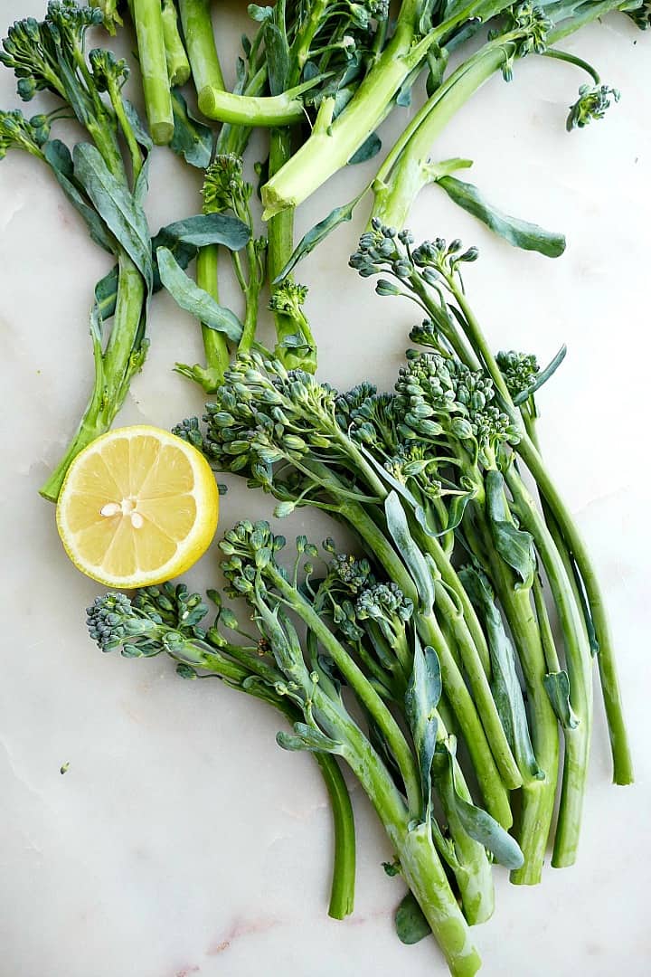 raw broccolini next to a sliced lemon scattered on a white counter