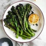 grilled broccolini and lemon in a white bowl on a napkin