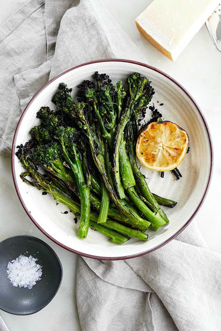 grilled broccolini and lemon in a white bowl on a gray napkin