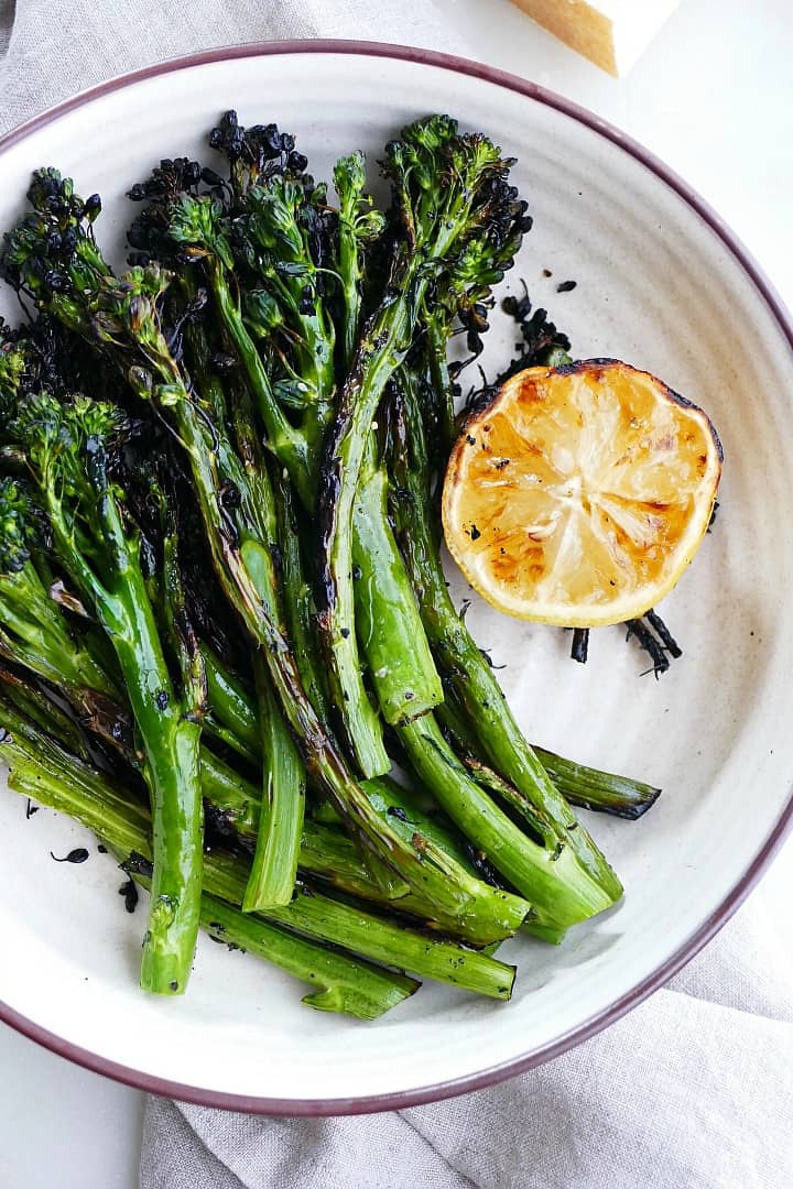 close up of grilled broccolini and lemon on a white bowl