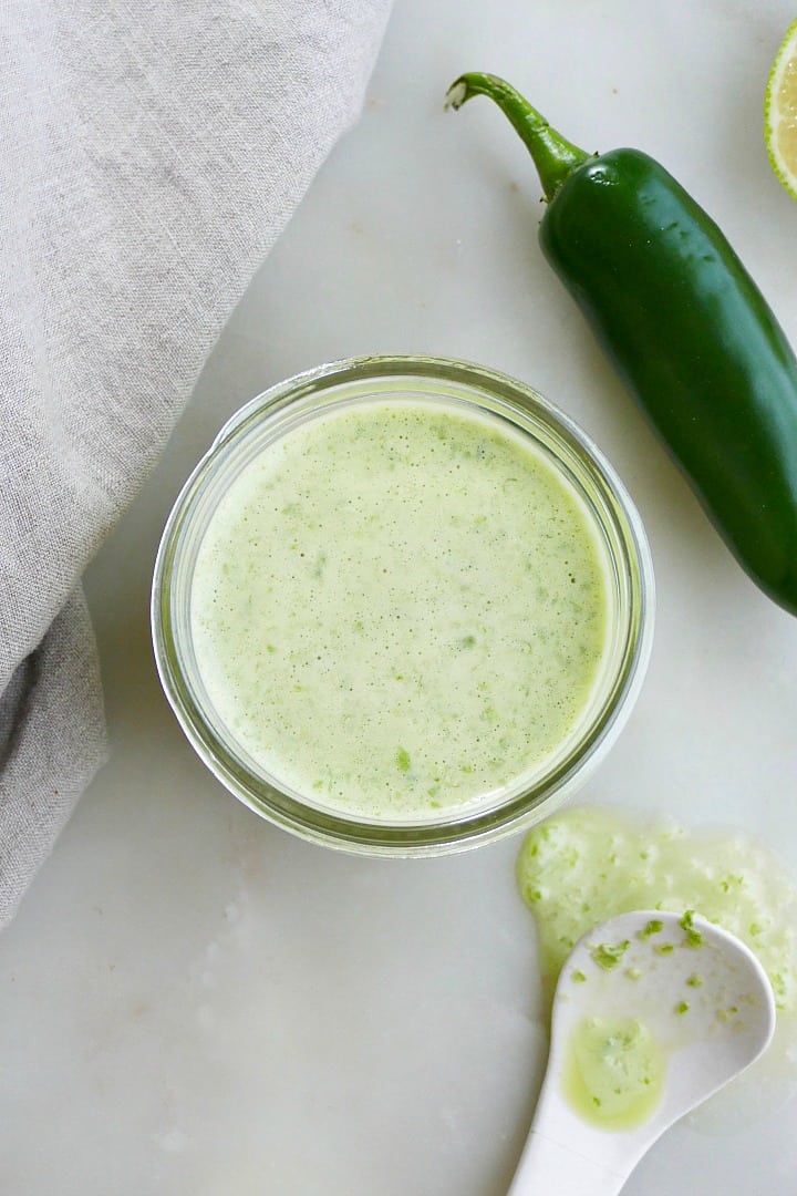 jalapeno lime dressing in a glass jar next to a napkin and spoon