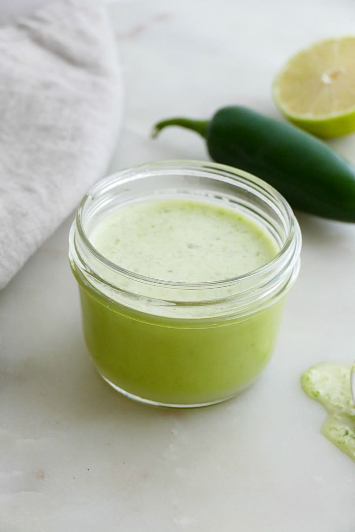 side angle of jalapeno lime dressing in a glass jar in front of a pepper