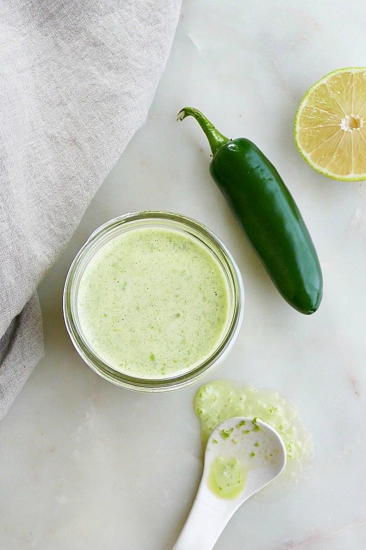 finished recipe in a jar next to a jalapeno, lime, spoon, and napkin