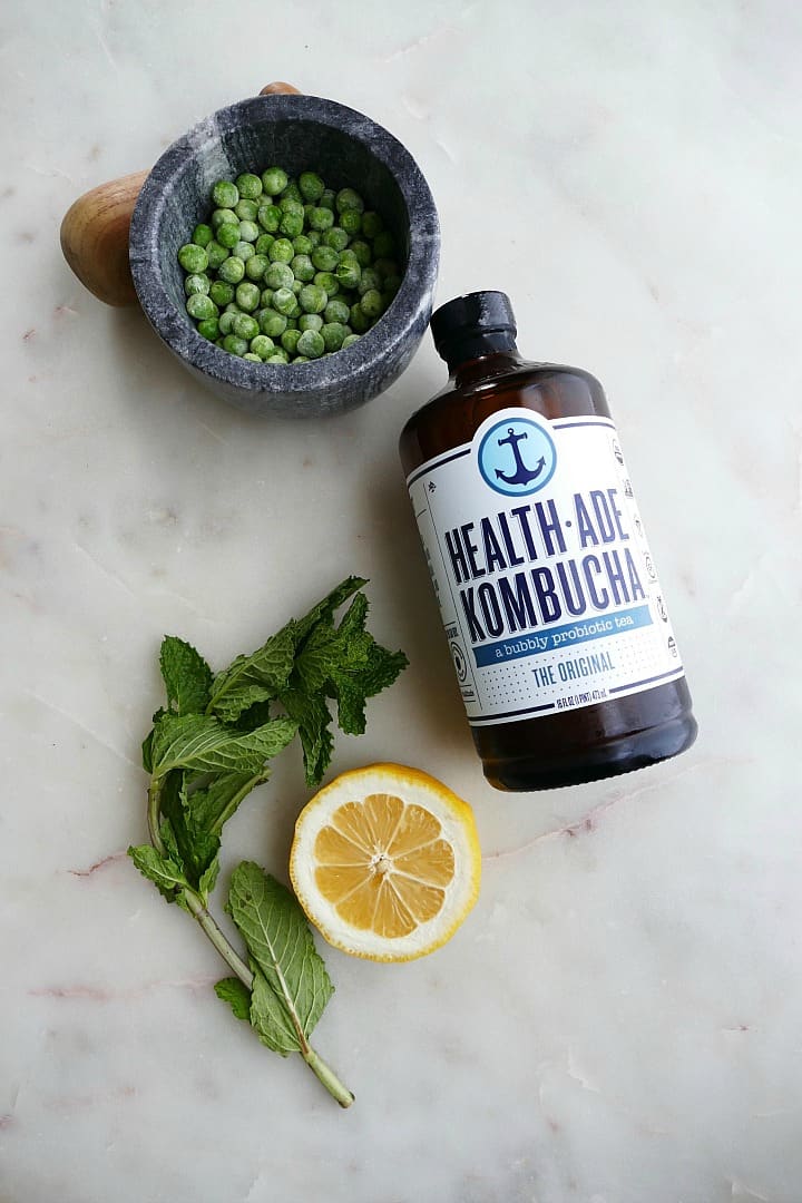 small bowl with frozen peas, bottle of original health-ade kombucha, a lemon, and mint leaves