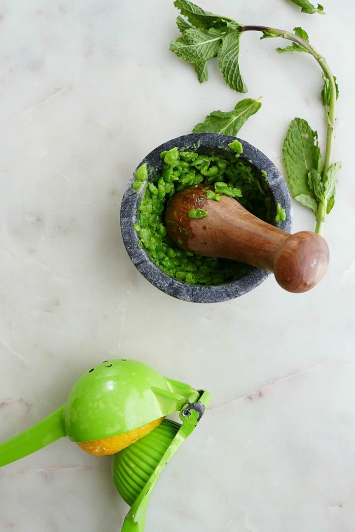peas muddled in a mortar and pestle next to a citrus squeezer
