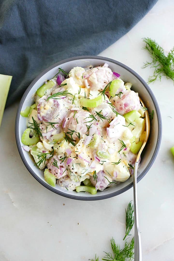 radish potato salad topped with fresh dill in a gray bowl with a spoon