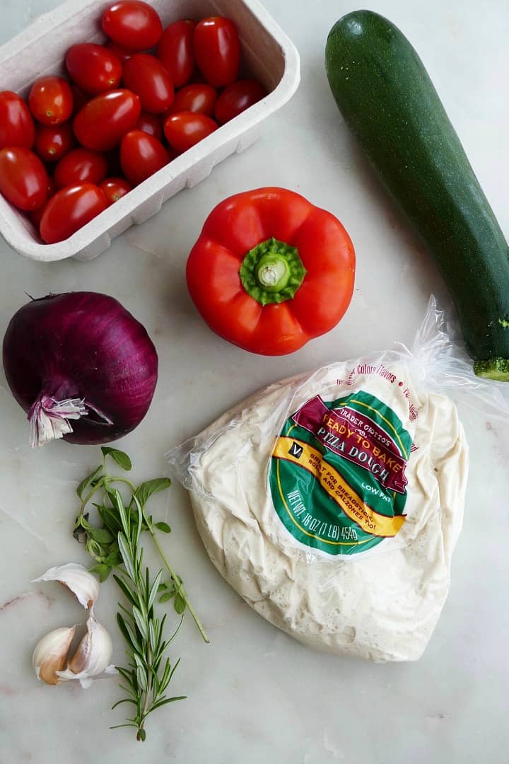 cherry tomatoes, bell pepper, onion, zucchini, pizza dough, garlic, and rosemary