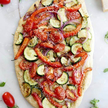 mediterranean roasted veggie flatbread on a white counter surrounded by ingredients