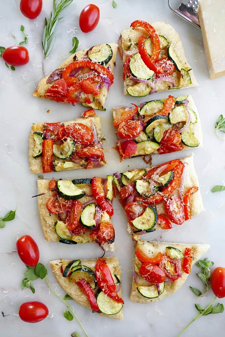 flatbread topped with tomatoes and summer veggies sliced into 8 pieces on a counter