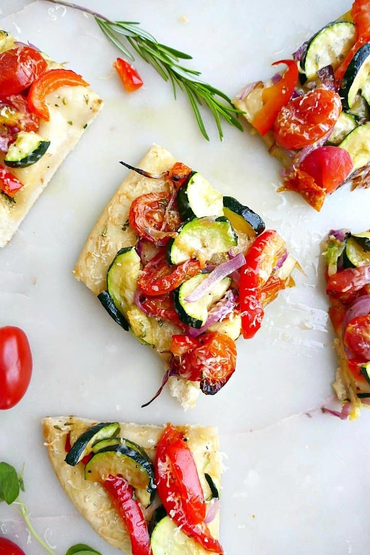 single square piece of veggie flatbread on a white counter next to other pieces