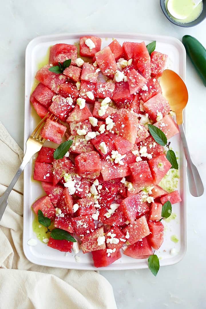 spicy watermelon salad with jalapeno dressing on a white rectangular platter