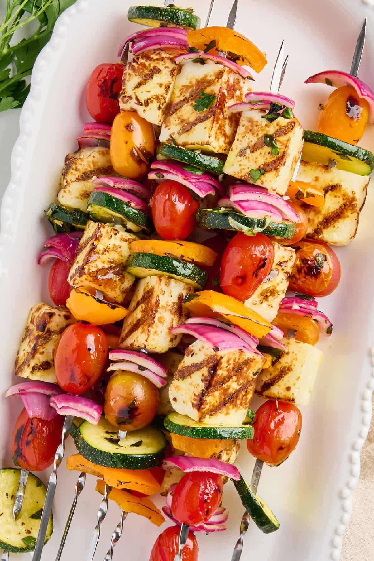 Vegetable and halloumi skewers with tomatoes on a white oval serving dish.