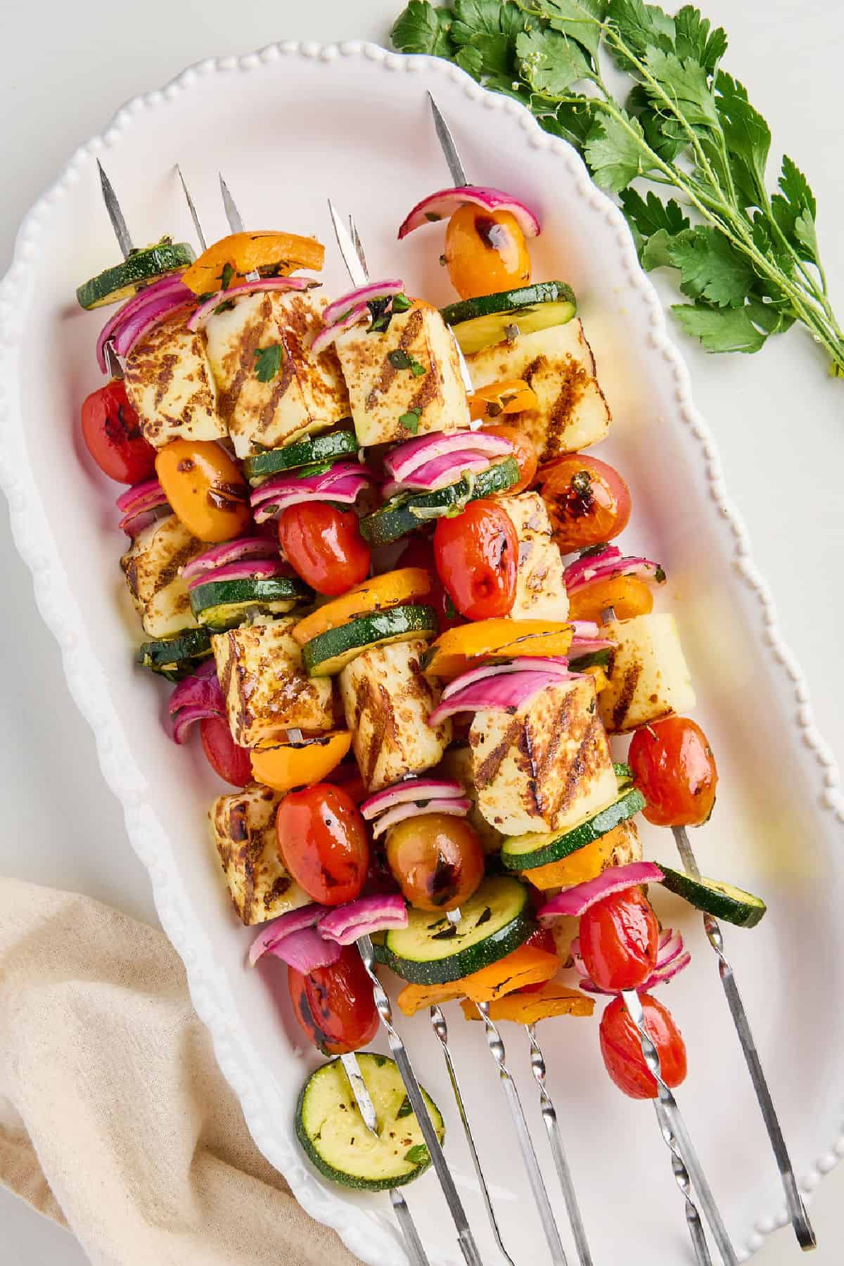 Halloumi, pepper, tomato, zucchini, and onion skewers on an oval serving dish.