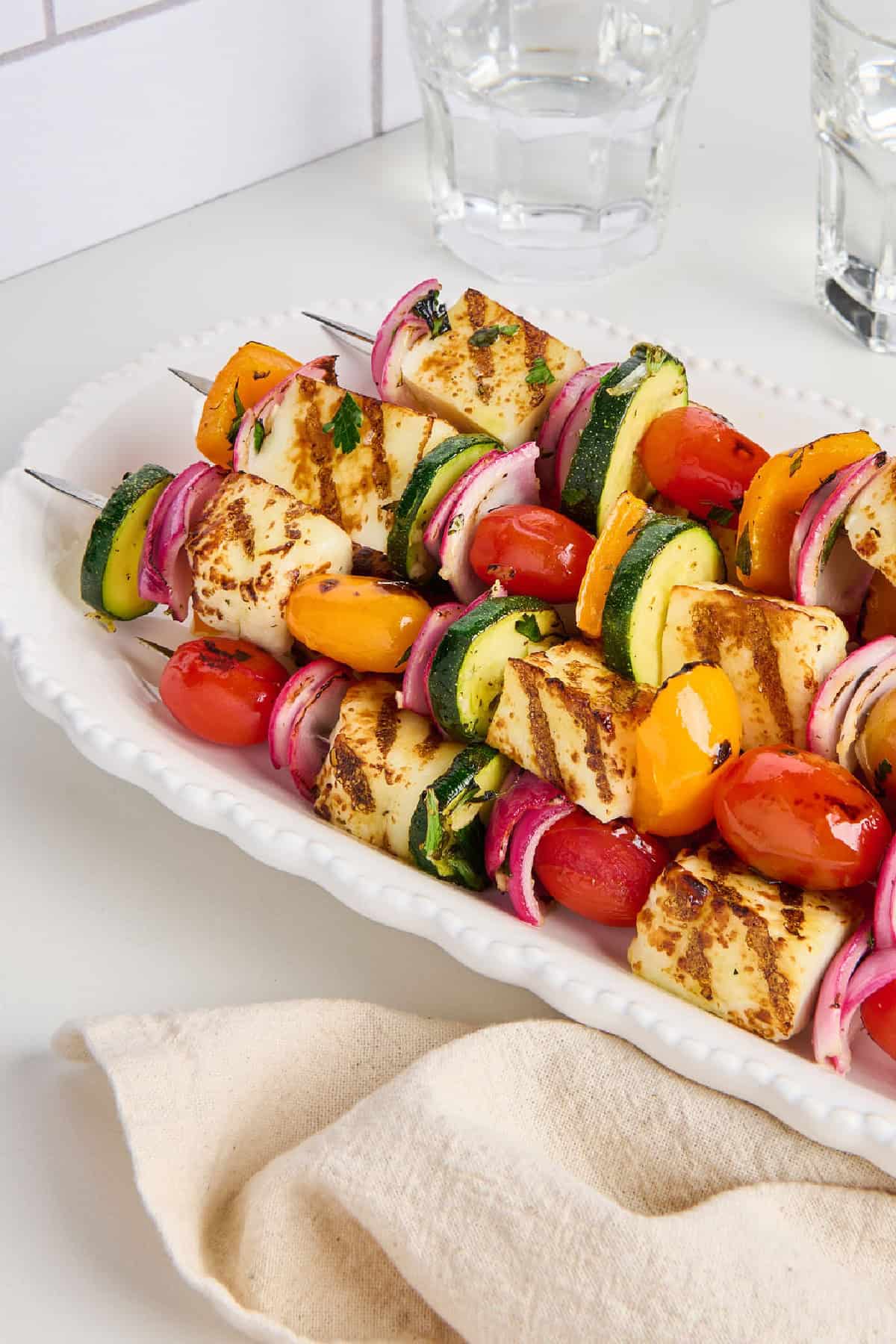 Vegetable skewers on a serving tray next to napkin and glasses of water.