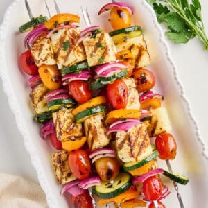 Veggie kabobs with halloumi cheese on a serving tray next to napkin and parsley.
