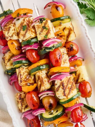 Veggie kabobs with halloumi cheese on a serving tray next to napkin and parsley.