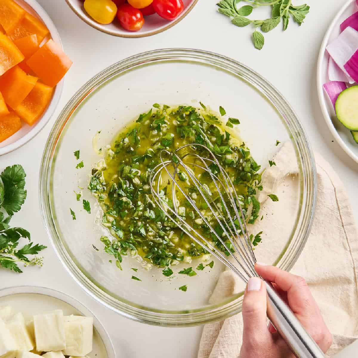 Woman whisking olive oil, garlic, and herb marinade for Mediterranean vegetable skewers.