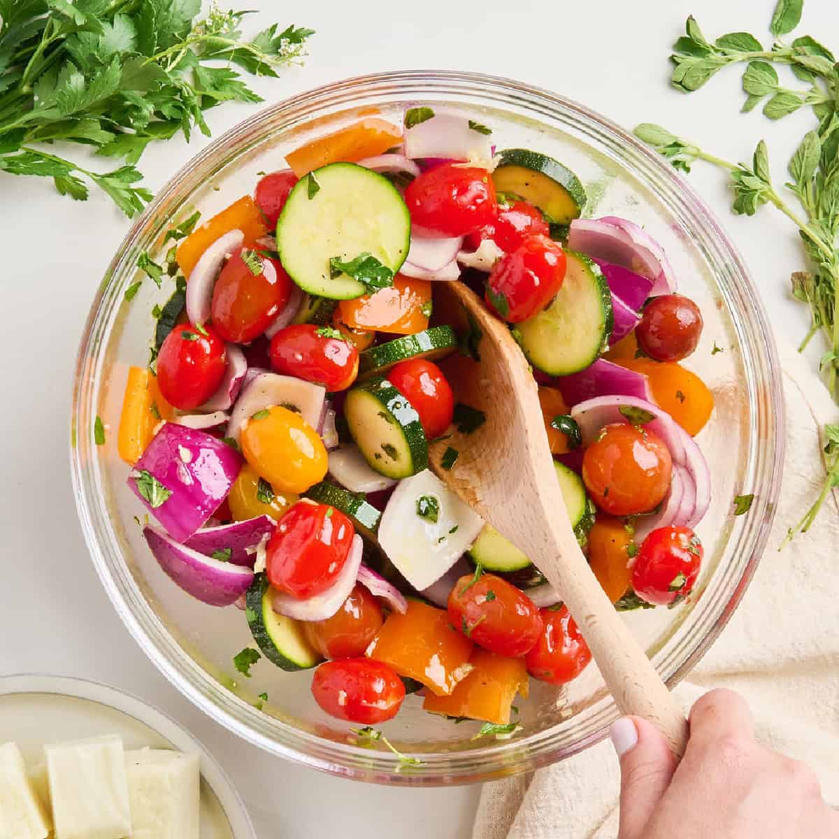 Woman stirring skewer vegetables and olive oil marinade together in a mixing bowl.