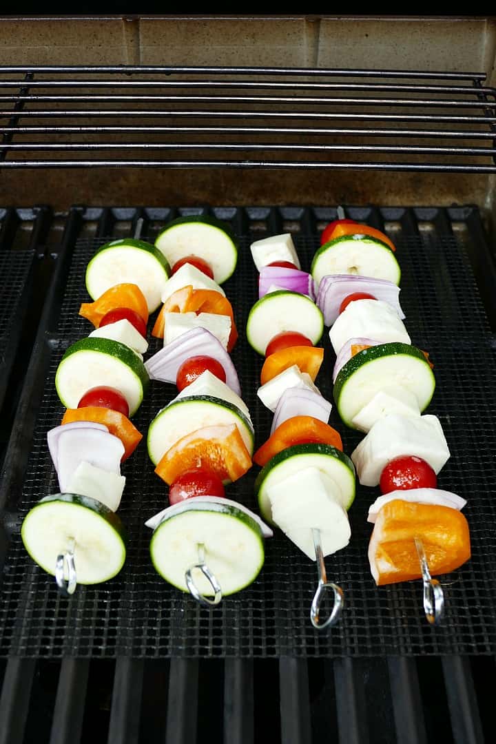 metal skewers with vegetables and halloumi on top of a mesh grill mat on a grill