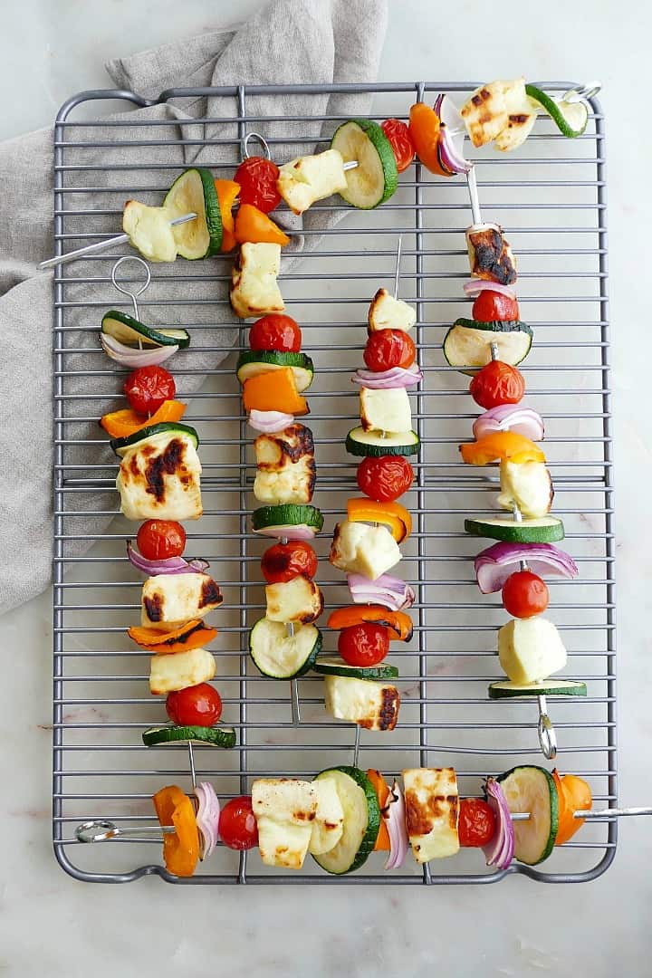 six vegetable skewers with halloumi on top of a metal cooling rack on a counter