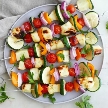 six grilled veggie and halloumi skewers on a serving plate on a counter