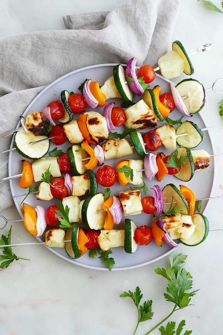 six grilled veggie and halloumi skewers on a serving plate on a counter