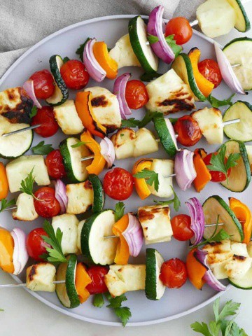 square image of six grilled veggie and halloumi kabobs on a serving plate