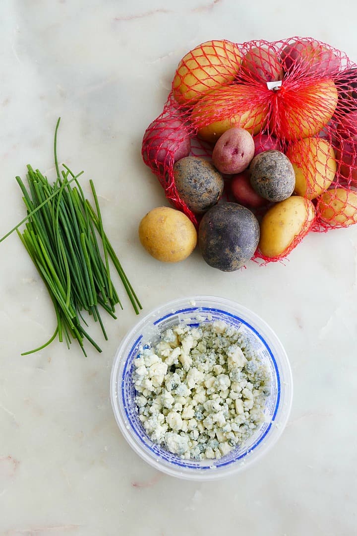 potato medley in a mesh bag next to chives and blue cheese on a counter