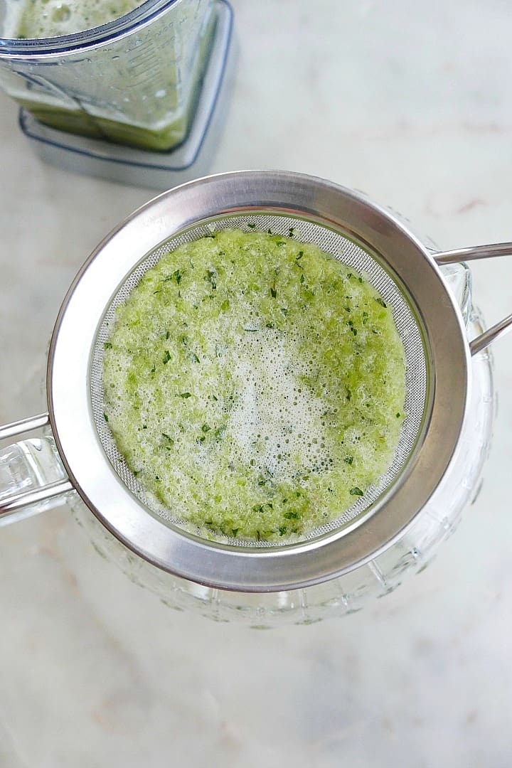 blended cucumber and mint straining through a sieve into a pitcher