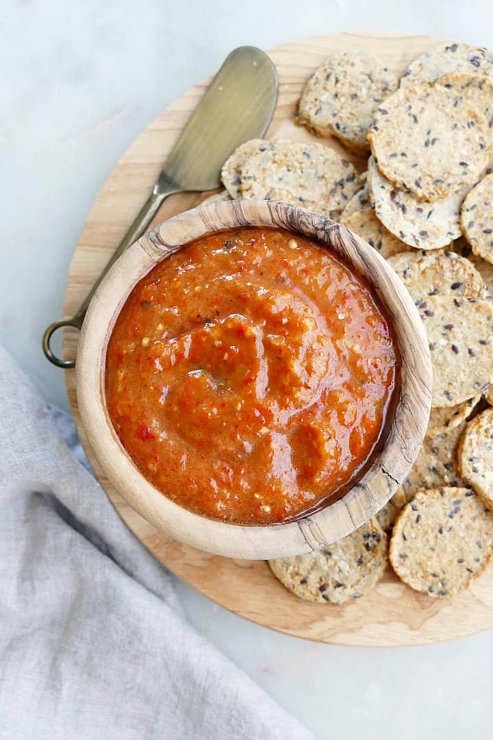 a wooden bowl with eggplant red pepper dip surrounded by crackers on a platter