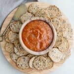 bowl of dip surrounded by seed crackers on a circular wooden serving board